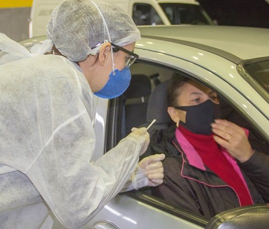 Santa Catarina registra 12.038 casos ativos de coronavírus profissional de saúde trajada com epi se inclina para janela de carro onde está mulher e homem com máscaras dentro do veículo