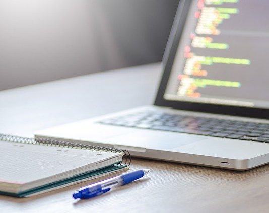 UFSC sofre ataque de hackers no primeiro dia de aulas online caderno e caneta em frente a um notebook com códigos na tela