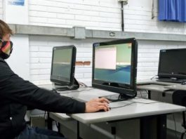 UFSC começa a distribuir computadores e paga primeiro auxílio para acesso à internet homem usando máscara sentado em frente a um computador em sala com mais computadores