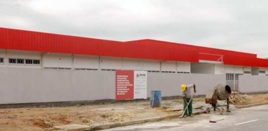 Construções das novas creches em São José avançam, na Av. Beira-mar parte externa de creche com operário retirando areia do meio fio e betoneira ao lado