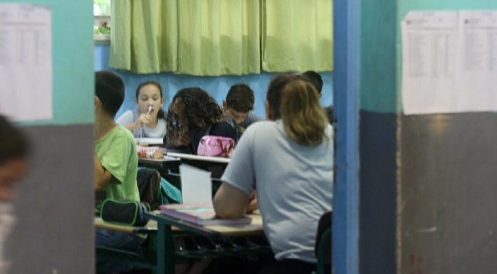 alunos vistos sentados nas carteiras de sala de aula por entre a porta