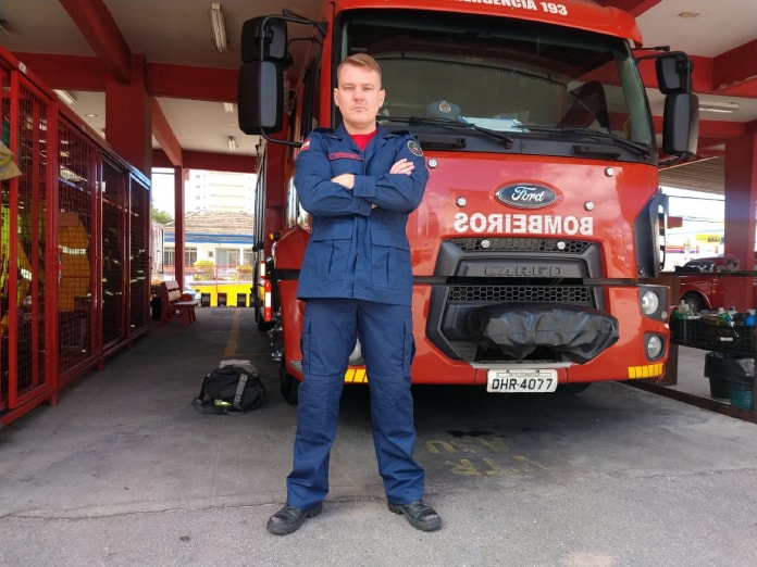Nelson Ariberto Borchardt com uniforme olha sério de braços cruzados para a foto em frente a um caminhão dos bombeiros
