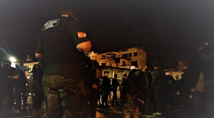 policiais em pé em foto noturna no pátio da delegacia; cachorro pastor alemão ao centro