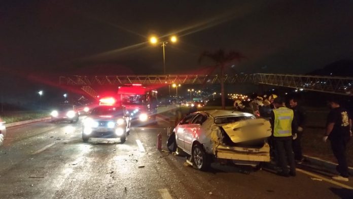 carro destruído em faixa da direita com outros carros passando ao lado em foto noturna