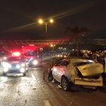 carro destruído em faixa da direita com outros carros passando ao lado em foto noturna