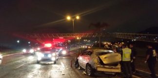 carro destruído em faixa da direita com outros carros passando ao lado em foto noturna