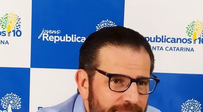 antônio lemos visto um pouco de lado; ele está de óculos e barba, usando uma camisa azul; atrás há um painel com logos do partido republicanos