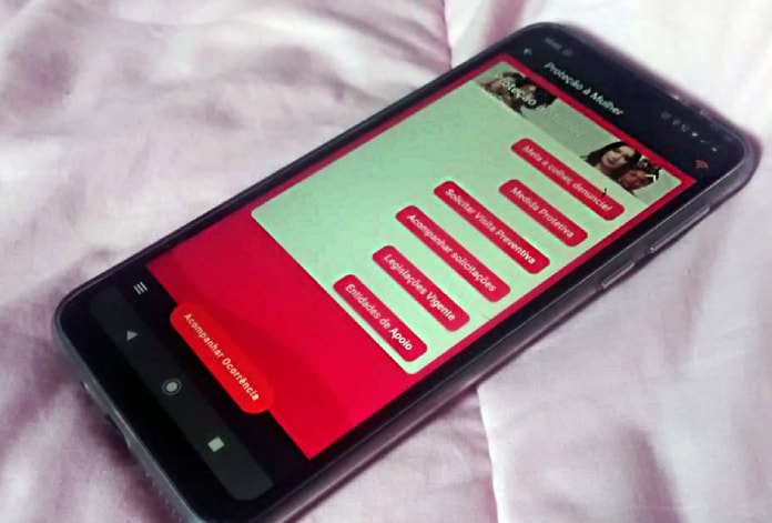 aplicativo pmsc aberto na tela de celular sobre cama; tela mostra sessão de proteção à mulher