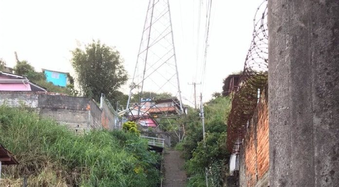 dois policiais do bope uniformizados vistos de costas em área do morro; torres de transmissão no alto