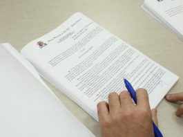 documento sobre a mesa com mãos em cima segurando caneta