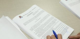 documento sobre a mesa com mãos em cima segurando caneta
