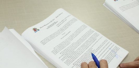 Mesa diretora da câmara de São José assina o novo Código de Obras documento sobre a mesa com mãos em cima segurando caneta