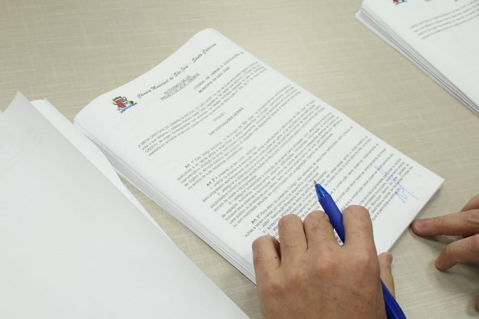 documento sobre a mesa com mãos em cima segurando caneta