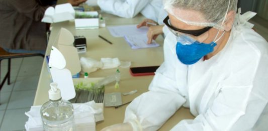 SC confirma 472 mil casos, 443 mil recuperados e 4.885 mortes por Covid profissional de saúde faz teste no dedo de pessoa com mão apoiada sobre mesa onde estão outros objetos