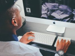 homem negro jovem visto de costas trabalhando em computador com dados na tela