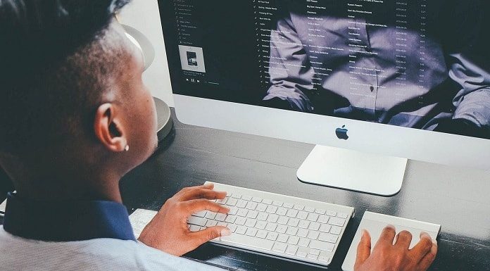 homem negro jovem visto de costas trabalhando em computador com dados na tela