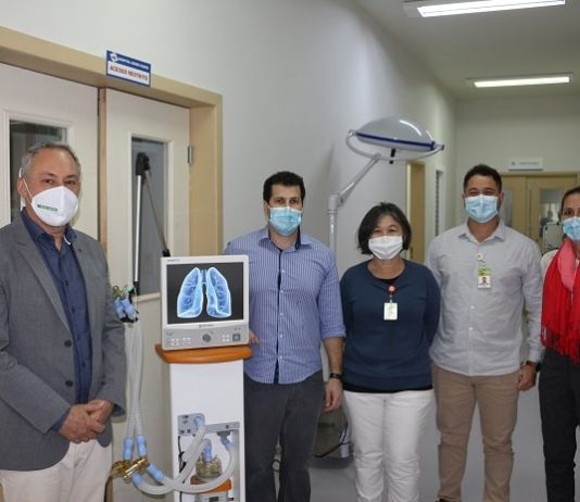 cinco pessoas usando máscara posam para a foto no corredor do hospital ao lado do respirador