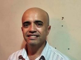 edson fortuna olha sorridente para a câmera; ele é careca e usa uma camiseta branca com listras