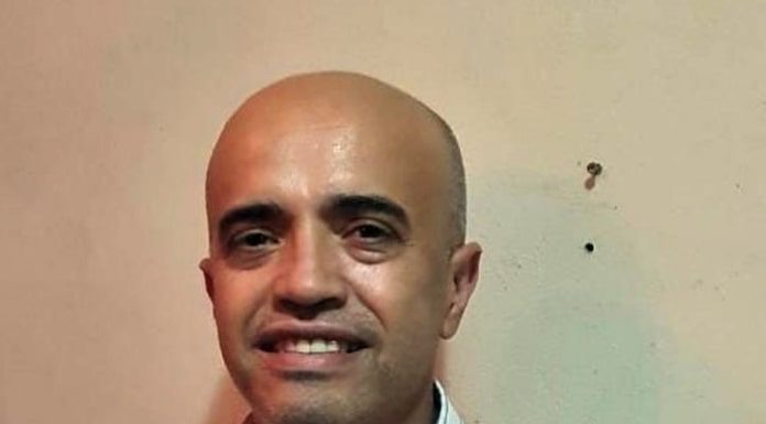 edson fortuna olha sorridente para a câmera; ele é careca e usa uma camiseta branca com listras