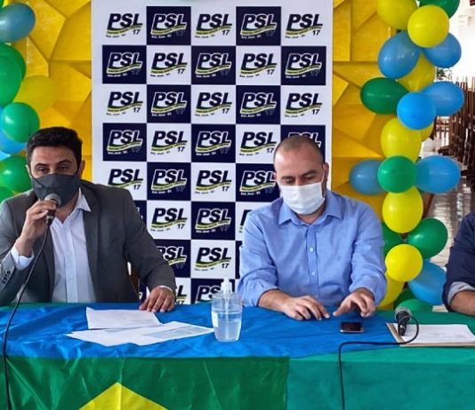 fernando anselmo sentado atrás de bancada com bandeira do brasil fala ao microfone; ele usa terno e máscara; ao lado sentados outros dois homens de máscara; ao fundo painel do partido com balões verdes, amarelos e azuis