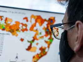 mulher usando máscara preta e óculos, olhando mapa na tela de computador