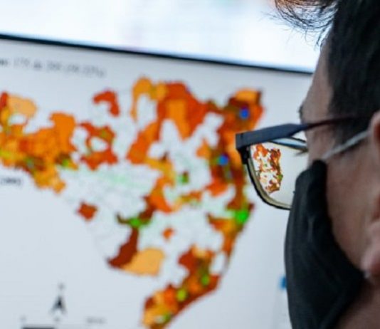 Municípios podem executar medidas de combate à pandemia sem prejuízo à atuação do Estado mulher usando máscara preta e óculos, olhando mapa na tela de computador