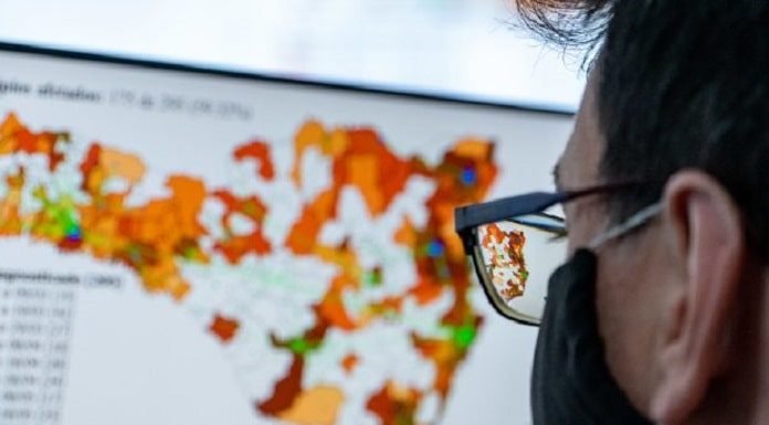 mulher usando máscara preta e óculos, olhando mapa na tela de computador