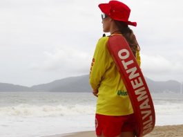 Abertas as inscrições em curso de guarda-vidas para temporada 2020/21 mulher com uniforme e boia de guarda-vidas vista de costas olhando para o mar