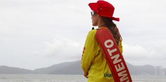 mulher com uniforme e boia de guarda-vidas vista de costas olhando para o mar