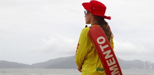 Três praias de Florianópolis recebem novos postos de guarda-vidas mulher com uniforme e boia de guarda-vidas vista de costas olhando para o mar