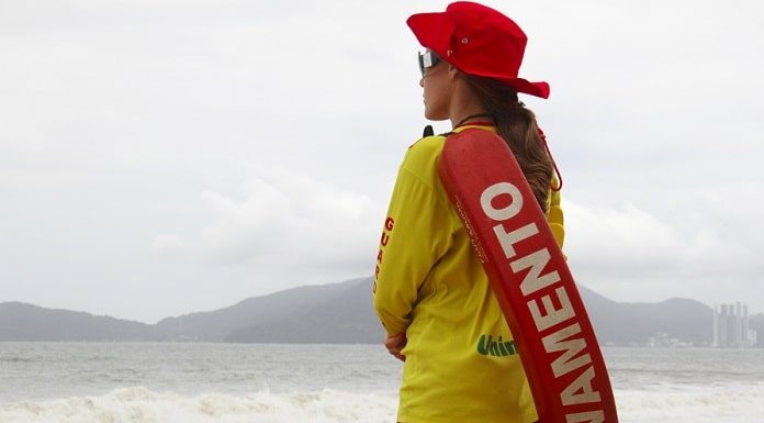 mulher com uniforme e boia de guarda-vidas vista de costas olhando para o mar