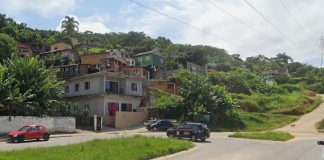 casas no morro entre vegetação vistas a partir no nível da avenida, com viaturas e outros dois carros estacionados