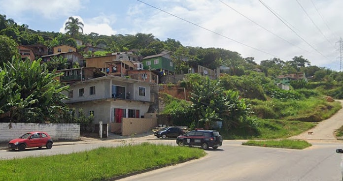 casas no morro entre vegetação vistas a partir no nível da avenida, com viaturas e outros dois carros estacionados