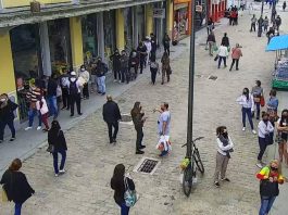 imagem de câmera de segurança sobre rua felipe schmidt no centro de florianópolis mostra pessoas espalhadas e andando pelo caldação, algumas paradas em frente aos comércios. todas de máscaras. poste no meio
