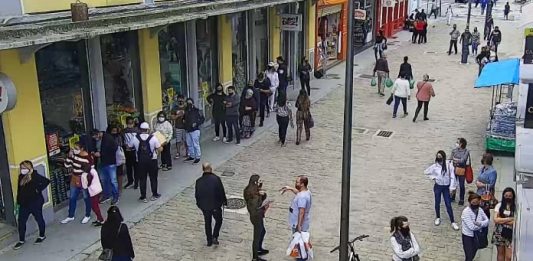 imagem de câmera de segurança sobre rua felipe schmidt no centro de florianópolis mostra pessoas espalhadas e andando pelo caldação, algumas paradas em frente aos comércios. todas de máscaras. poste no meio