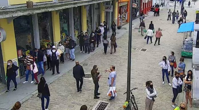 imagem de câmera de segurança sobre rua felipe schmidt no centro de florianópolis mostra pessoas espalhadas e andando pelo caldação, algumas paradas em frente aos comércios. todas de máscaras. poste no meio