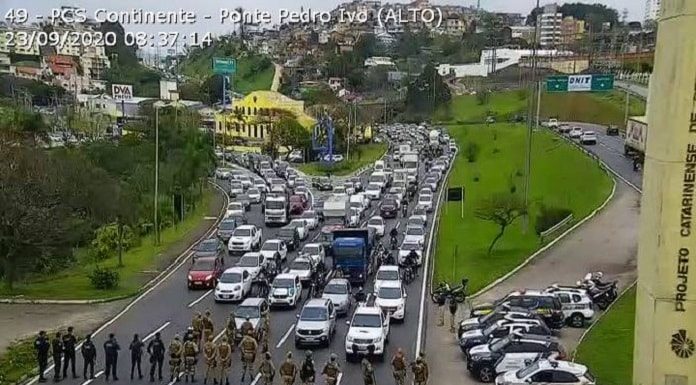 linha de policiais em pé cruzando barreira na pista e grandes filas paradas na via expressa