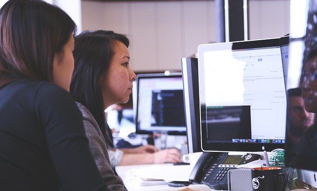 Duas mulheres sentadas a esquerda, de frente para um computador a direita