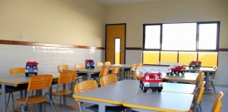 sala de aula com carteiras e cadeiras organizadas com caminhão de brinque sobre a mesa