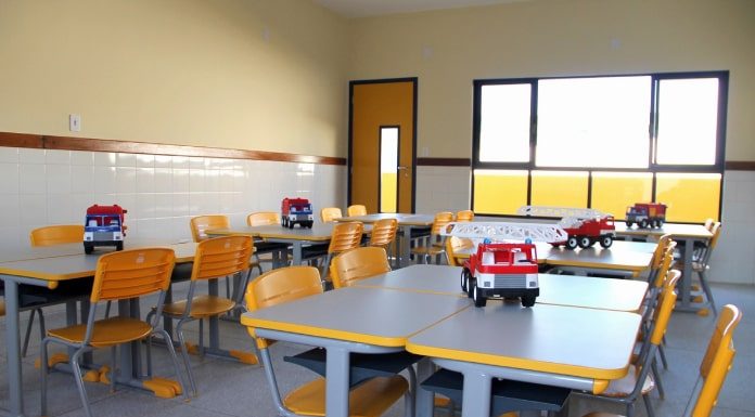 sala de aula com carteiras e cadeiras organizadas com caminhão de brinque sobre a mesa