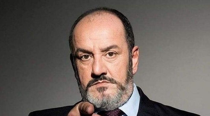 roberto salum olhando para a foto e apontando direto para a câmera; ele usa um terno preto e gravata bordô