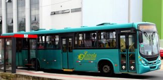 ônibus verde da empresa estrela visto de lado parado em frente a ponto de ônibus com algumas pessoas