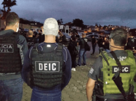 policiais civis vistos de costas aglomerados em estacionamento; inscrição deic nas costas