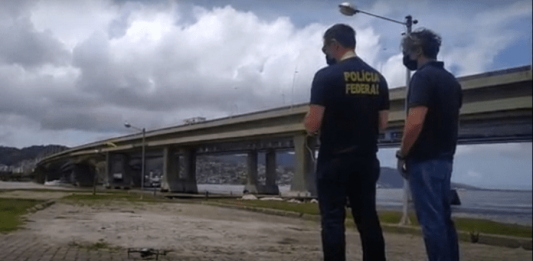 Polícia Federal utilizará drones para fiscalizar as eleições de 2020 dois policiais federais de costas olham para drone no céu ao lado das pontes de florianópolis