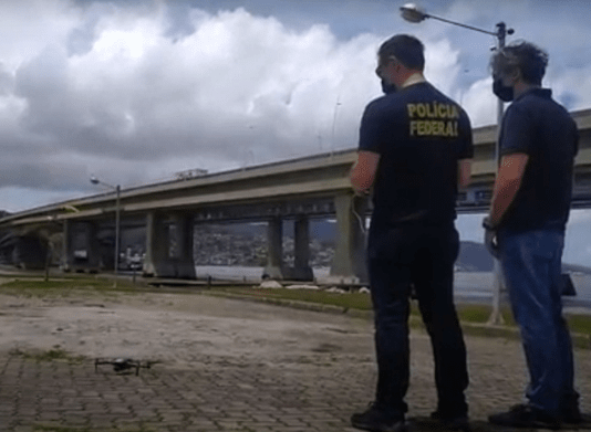Polícia Federal utilizará drones para fiscalizar as eleições de 2020 dois policiais federais de costas olham para drone no céu ao lado das pontes de florianópolis