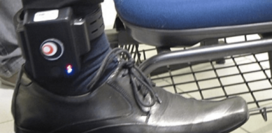 tornozeleira em perna de homeom com calça, sapato e meias sociais com o pé sobre uma cadeira