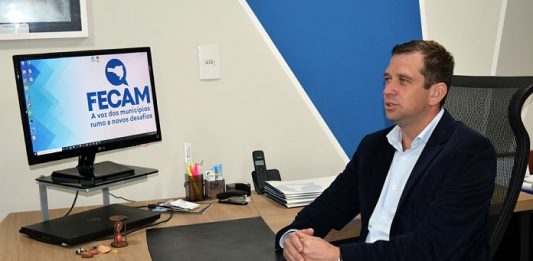 paulo weiss fala sentado atrás de mesa de escritório onde há computador com logo da fecam; ele está de lado, usando blazer