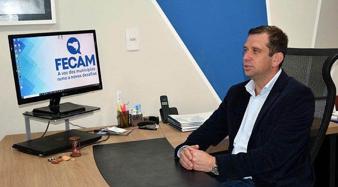 paulo weiss fala sentado atrás de mesa de escritório onde há computador com logo da fecam; ele está de lado, usando blazer