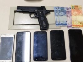 revolver, cinco celulares e 34 reais apreendidos sobre uma mesa