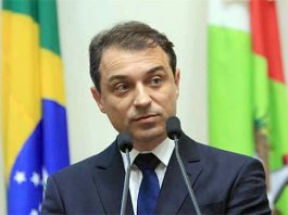 carlos moisés falando em dois microfones com bandeiras de brasil e sc ao fundo